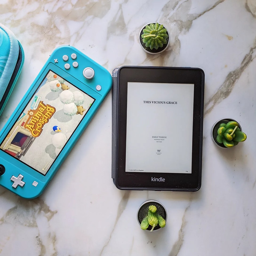 A Kindle rests on a marble table next to a Nintento Switch with Animal Crossing, surrounded by cactus/succulent votive candles