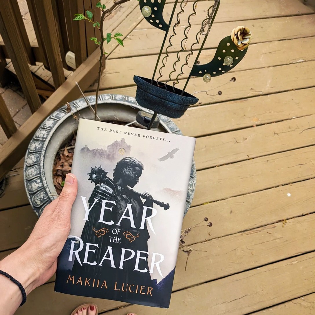 Alexis holds Year of the Reaper in front of a plant and a solar-powered metal cactus.