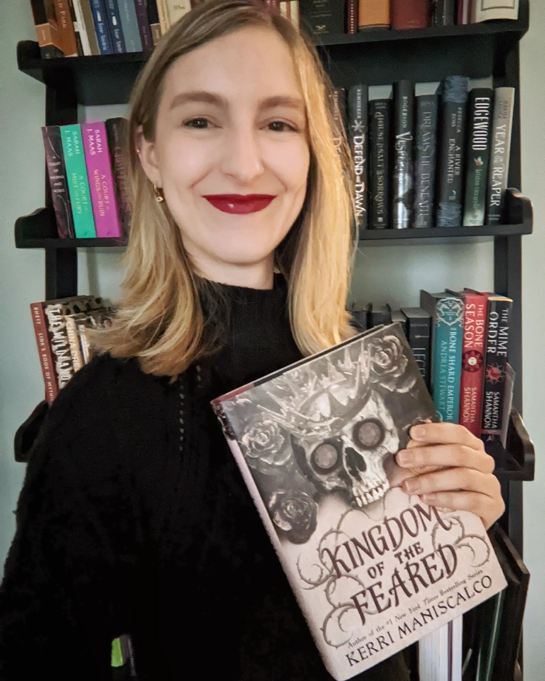 Alexis holds Kingdom of the Feared in front of a bookshelf