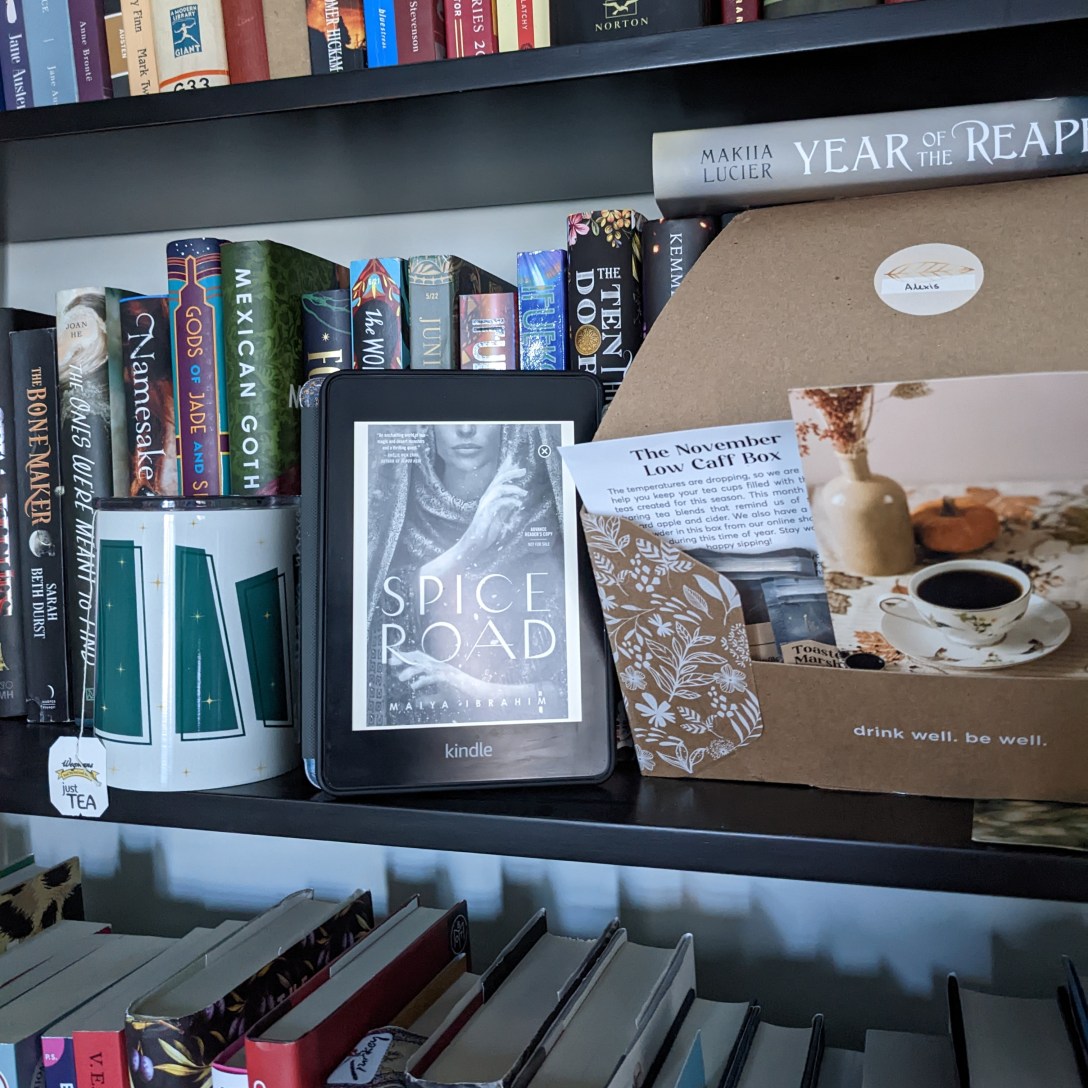 A Kindle copy of Spice Road sits on a bookshelf next to a tea tumbler and a box of tea samplers.