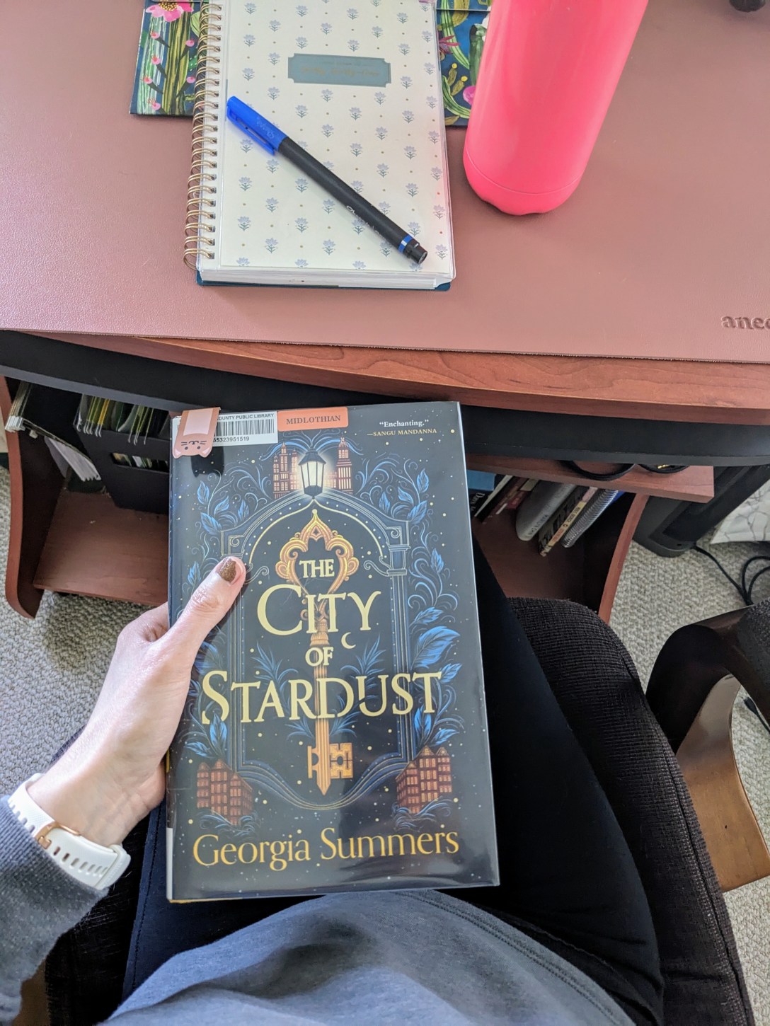 The City of Stardust in front of a desk with a planner and a pink water bottle