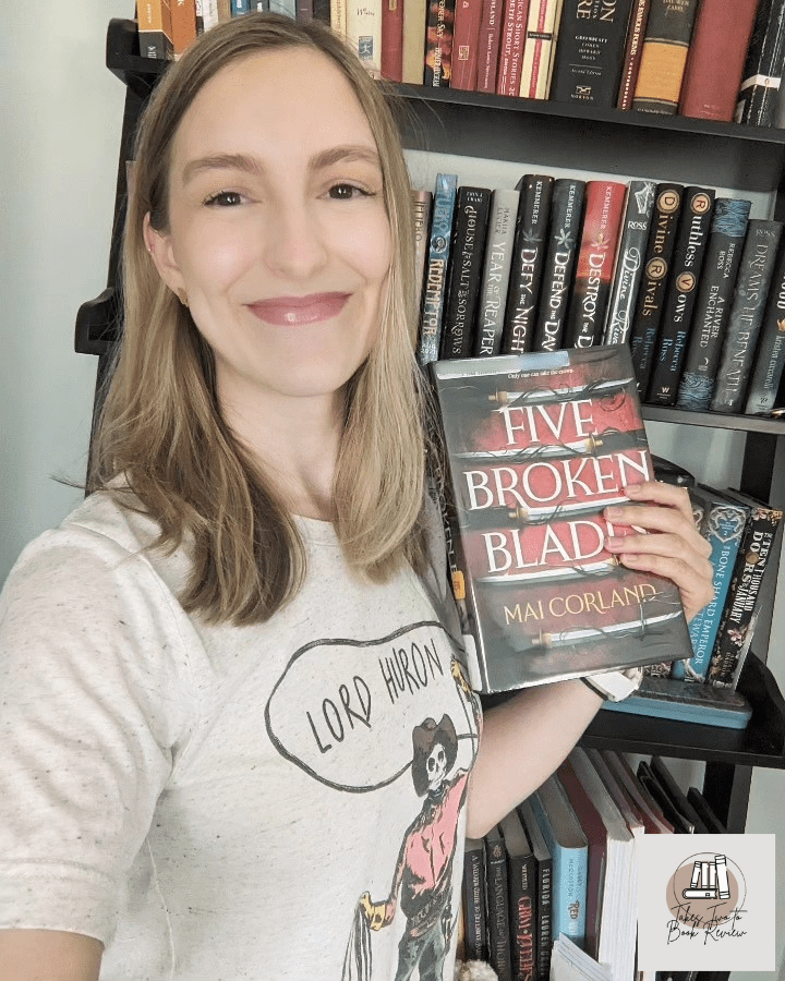 Alexis holds Five Broken Blades in front of a bookshelf