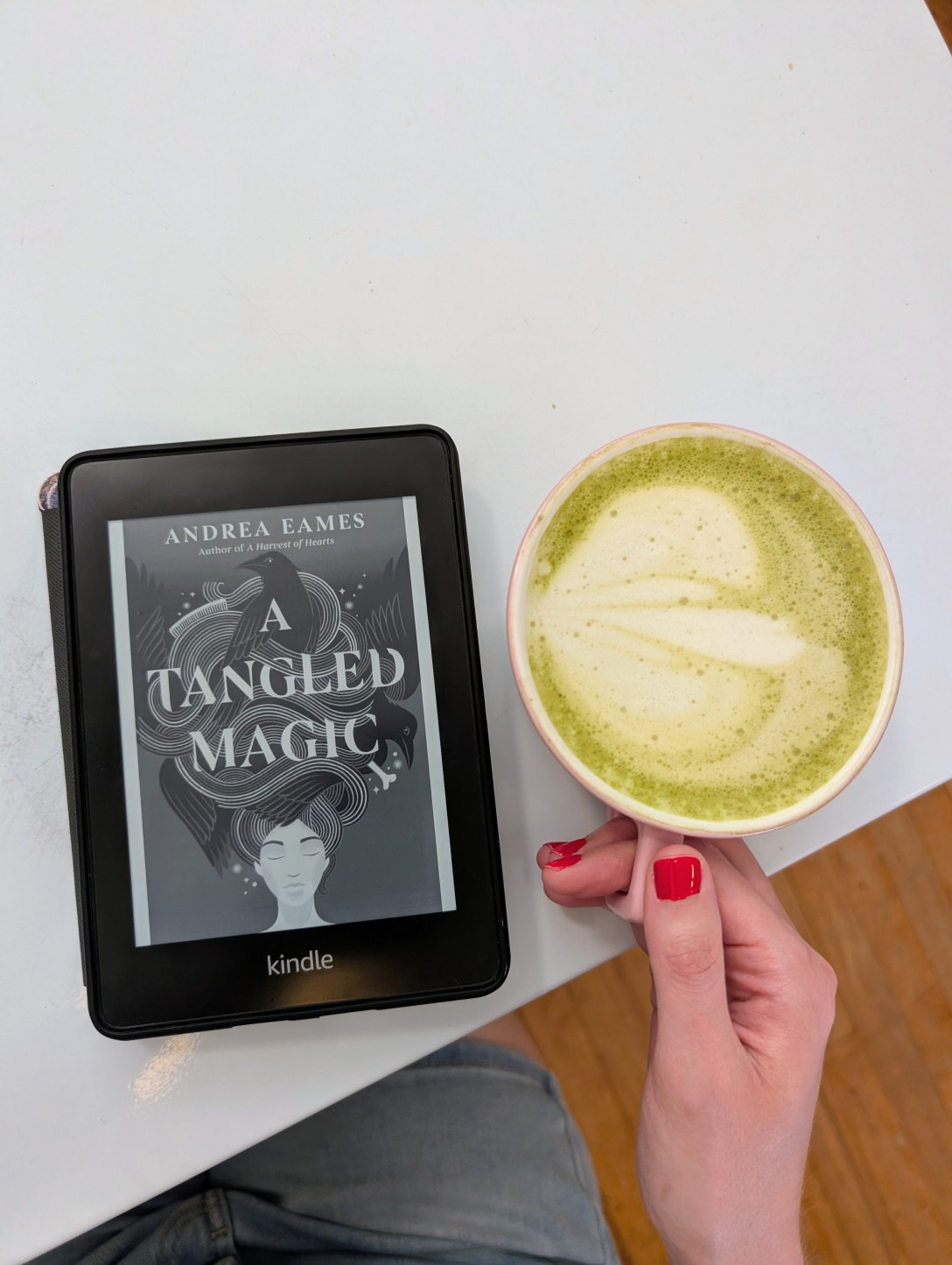 A Kindle with A Tangled Magic book cover and a blueberry matcha latte in a mug